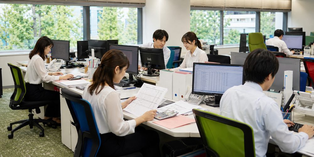 伝票や資料を確認しながら電卓とPCで会計処理を進める経理スタッフ