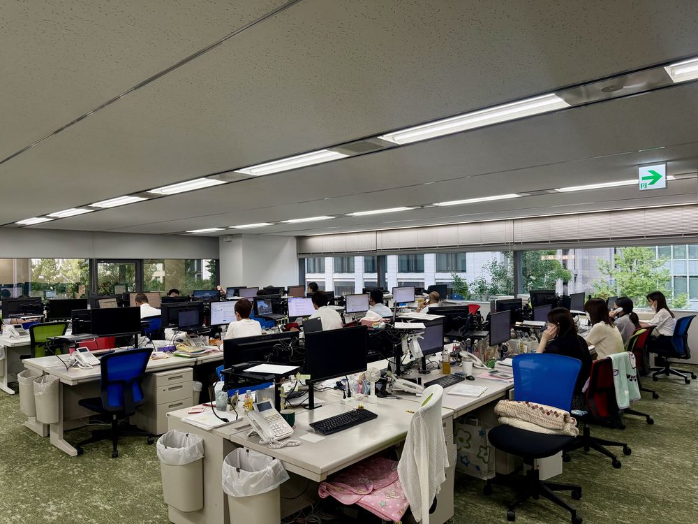 大阪本社の開放的なオープンオフィス。窓から自然光が入る執務スペースで働く社員たち